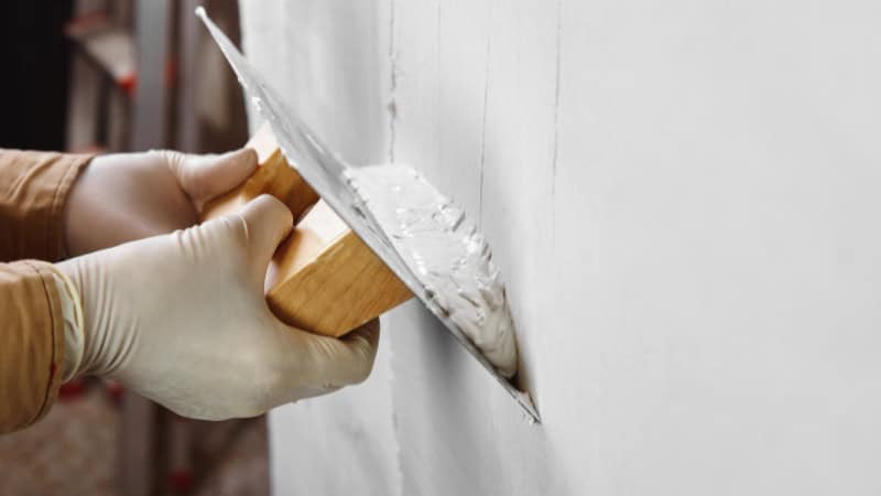 Un peintre qui applique de l'enduit sur un mur d'une maison à Chatou